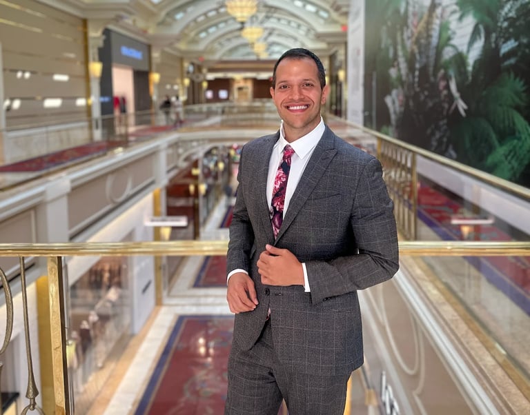 Man in gray suit smiling while standing on a mall balcony overlooking multiple levels below